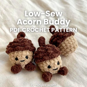 May include: Three crocheted acorn buddies with smiling faces and small arms. The acorns have a light brown body and a dark brown cap. The text "Low-Sew Acorn Buddy PDF Crochet Pattern" is displayed in white.