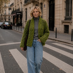 Puede incluir: Un cárdigan de ganchillo abierto de color verde brillante con un patrón de cuadrados texturizados y bordes acanalados, sobre una camiseta gris de manga larga con cuello alto, combinado con vaqueros azul claro, zapatillas deportivas grises y bolso marrón.