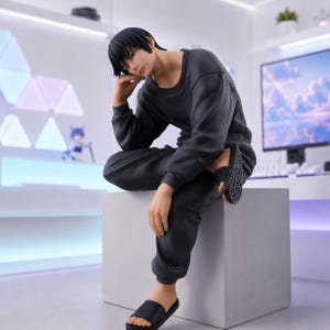 May include: A collectible anime-style figure of a character with short black hair, wearing a long-sleeved dark gray sweatshirt and matching sweatpants. The figure is seated on a light gray cube, wearing black slide sandals on their feet.