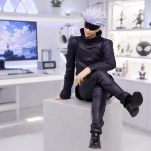 May include: A collectible anime figure of a character with spiky white hair and a black blindfold over their eyes. The figure wears a dark navy blue high-collared jacket and matching trousers, sitting in a relaxed pose on a light gray cube base.
