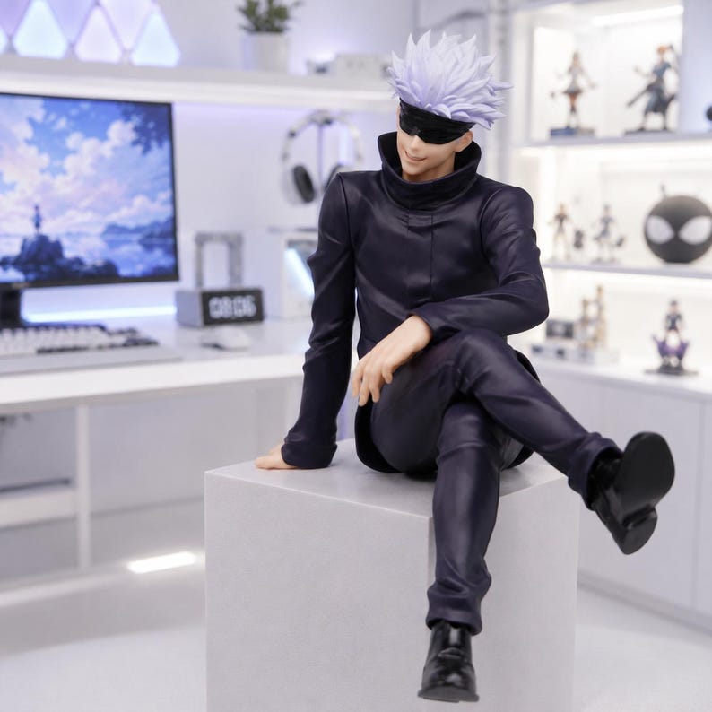 May include: A collectible anime figure of a character with spiky white hair and a black blindfold over their eyes. The figure wears a dark navy blue high-collared jacket and matching trousers, sitting in a relaxed pose on a light gray cube base.