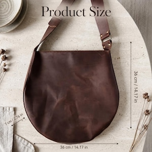 May include: A dark brown leather shoulder bag with a wide strap and metal hardware. The bag features dimensions of 14.17 inches in height, 14.17 inches in width, and 2.76 inches in depth, as indicated by the text Product Size and measurements.