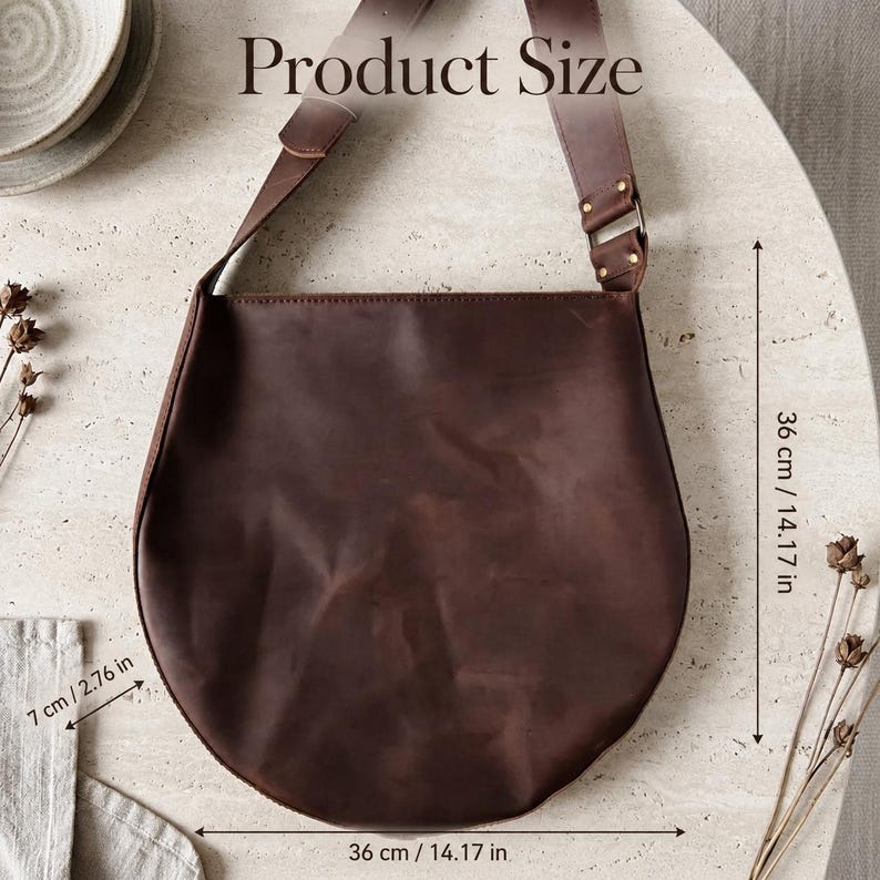 May include: A dark brown leather shoulder bag with a wide strap and metal hardware. The bag features dimensions of 14.17 inches in height, 14.17 inches in width, and 2.76 inches in depth, as indicated by the text Product Size and measurements.