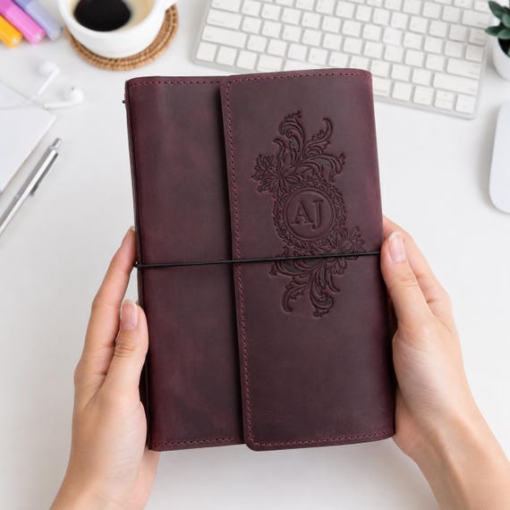 A trifold leather traveler's notebook with 6 elastic bands, zipper pocket, pen loop, and custom floral monogram — wildly functional and genuinely beautiful craft.