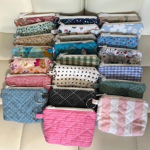 May include: A collection of small, quilted coin purses in various colors and patterns. Designs include floral, polka dots, gingham, and geometric shapes. Each purse has a zipper closure and a small metal ring.