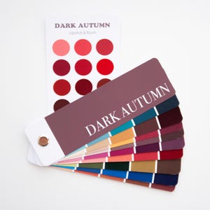 May include: A color palette fan with the text "DARK AUTUMN" and a separate card with lipstick and blush color swatches. The palette features a range of colors, including reds, pinks, and various shades of other colors.