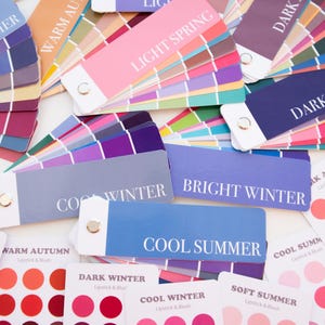 May include: A collection of color palette cards for seasonal color analysis. The cards display a range of colors, including pinks, blues, purples, and greens. Text on the cards includes "Soft Summer," "Light Spring," "Cool Winter," and "Bright Winter."