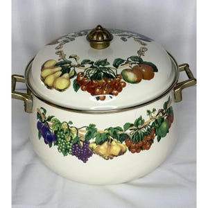 May include: Cream-colored enamel pot with a lid, adorned with a vibrant fruit garland design. The pot features brass-toned handles and a matching knob on the lid. The fruit includes pears, apples, grapes, and cherries.