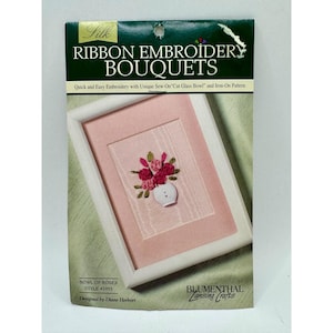 May include: A craft kit for ribbon embroidery, featuring a framed floral design. The kit includes a pink background with a white frame, and the text "RIBBON EMBROIDERY BOUQUETS". The design showcases a vase of red and pink roses. The kit is designed by Diane Herbort.
