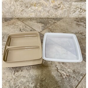 Könnte beinhalten: Zwei Kunststoff-Lebensmittelbehälter. Einer ist beige mit zwei Fächern, der andere ist weiß mit quadratischer Form. Die Behälter sind leer und bereit zum Befüllen. Auf einer Steinoberfläche.