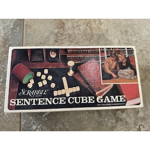 May include: A vintage Scrabble Sentence Cube Game box. The box has a dark background with game pieces, books, and a photo. The game's title is displayed. The box also includes an image of a couple playing the game.