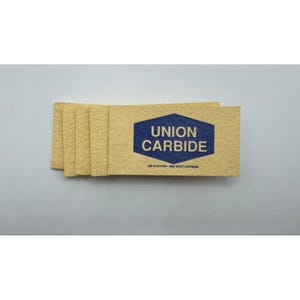 Puede incluir: Un montón de tarjetas rectangulares de color marrón claro. Cada tarjeta tiene las palabras "UNION CARBIDE" en un hexágono azul, con el texto "DIP IN WATER - SEE WHAT HAPPENS" debajo.