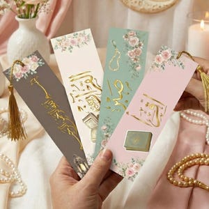 May include: Four decorative bookmarks with floral and gold accents. Each bookmark features a different design, including calligraphy and illustrations. The bookmarks are held in a person's hand, with a gold tassel attached to each.