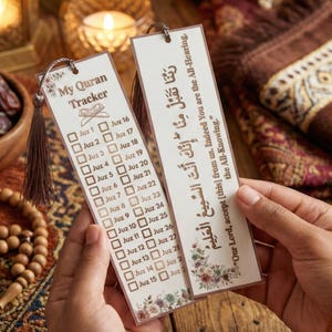 May include: Two rectangular Quran trackers are held in hands. The trackers have a floral design at the bottom and a tassel. One tracker says "My Quran Tracker" and has check boxes. The other has Arabic text.