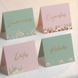 Pode incluir: Quatro cartões dobrados com texto dourado. Dois são verde-sálvia, dois são rosa. Os cartões verdes dizem "Sandwiches" e "Kababs". Os cartões rosa dizem "Cupcakes" e "Dates". Desenhos florais na parte inferior.