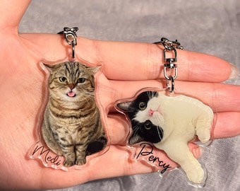 Peut inclure: Deux porte-clés en forme de chat. L'un présente un chat tigré avec le nom "Medi" imprimé. L'autre présente un chat noir et blanc avec le nom "Percy" imprimé. Les deux porte-clés ont des anneaux argentés.