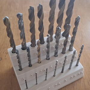 May include: A selection of metal drill bits in a light grey tiered holder, sizes from 1 to 9.5. The drill bits have a spiral design. The holder is labelled with the drill bit sizes in millimetres.