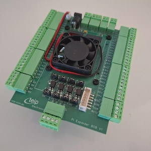 Può includere: Una scheda a circuito stampato verde con numerosi connettori verdi, una ventola nera e vari componenti elettronici. La scheda presenta il testo "teip.com.au" e "PI Expander BOB V1". Sono visibili fili che collegano i componenti.