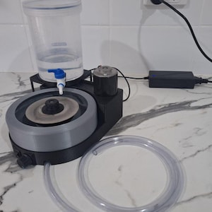 May include: A black and gray lapidary machine featuring a circular grinding disc, a clear plastic water reservoir with a blue valve, a motor, and a long, flexible, transparent plastic hose. The device includes a black power adapter with a cord.
