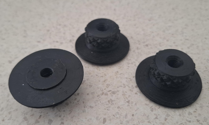 May include: Three black circular knobs with a flat base and a raised, textured cylindrical centre featuring a diamond-patterned grip. Each knob has a central threaded hole, showing a consistent design and matte finish across all three pieces.