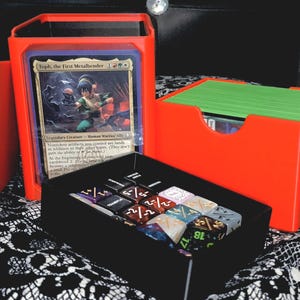 May include: A white ceramic mug with a black handle and the text "But First, Coffee" in a bold, black font. The mug is set against a blurred background, suggesting a cozy setting.