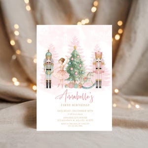 May include: A pink and white invitation card with a Christmas theme. The card features a ballerina, nutcrackers, a Christmas tree, and the text "Annabelle's First Birthday". The invitation is decorated with snowflakes and gift boxes.