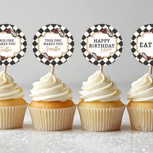 May include: Four cupcakes with white frosting and decorative toppers. The toppers have a black and white checkered pattern with text that reads "This One Makes You Taller", "This One Makes You Smaller", "Happy Birthday Olivia", and "Eat Me".