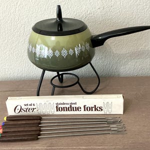 May include: A vintage fondue set with a green and black pot, black handle, and stand. Includes a box of six stainless steel fondue forks with wooden handles and colored tips. The pot has a white floral pattern.