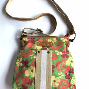 May include: A green, yellow, orange, and red floral print crossbody bag with a beige and white striped strap. The bag has a brown leather flap with the word "Levi's" embossed on it.