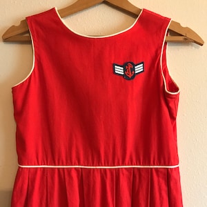 May include: A red sleeveless dress with a white trim and a blue and white anchor patch.