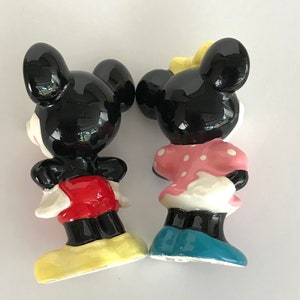May include: A ceramic figurine set of Mickey Mouse and Minnie Mouse. Mickey is wearing red shorts and yellow shoes. Minnie is wearing a pink polka dot dress and blue shoes.