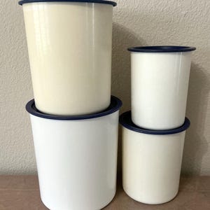 May include: Four enamelware canisters in varying sizes, stacked. The canisters are off-white with navy blue rims and lids. The arrangement shows a mix of sizes, offering a glimpse of the set's versatility for kitchen storage.