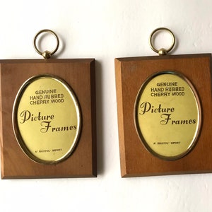 May include: Two wooden signs with gold oval frames and brass hangers. The signs advertise "Genuine Hand Rubbed Cherry Wood Picture Frames" with the text "A' Bristol Import".