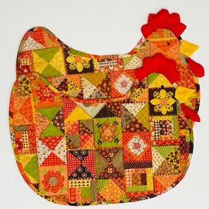 May include: A colorful, patchwork chicken-shaped kitchen item. The item features a vibrant mix of orange, yellow, green, and brown fabric squares. The chicken has a red comb and wattle. This decorative item is likely a trivet or kitchen decor.