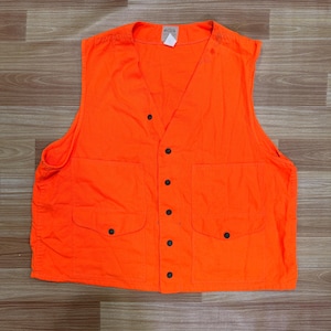May include: Bright orange vest with a V-neck, two front pockets, and black button closures. The vest has a label at the top and is made of a durable fabric. The vest is designed for outdoor activities.