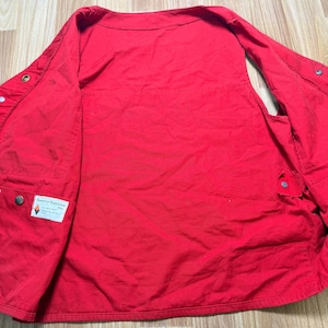 May include: A vibrant red vest featuring several pockets and button fastenings. The vest includes a collar and a label that reads "Forestry Suppliers Inc."