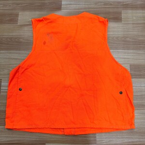 May include: Bright orange vest with two black buttons on the front. The vest is sleeveless and has a simple design. There is a small stain on the upper back of the vest. The vest is made of a durable material.