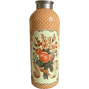 May include: A vintage-style talcum powder bottle with a silver cap. The bottle has a peach-colored background with a repeating cross pattern. A floral bouquet with roses and other flowers is displayed on the front, with the words "M. Fleurs" and "Talcum" on ribbons.