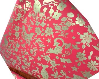 May include: Red wrapping paper with a gold floral and animal pattern. The design includes deer, birds, flowers, and stars. The paper is rolled up, showing the repeating pattern.