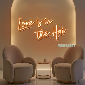 Pu&ograve; includere: Scena d'interni moderna con due poltrone beige, un tavolino rotondo e un'insegna al neon con la scritta "Love is in the Hair". L'insegna &egrave; in un carattere corsivo e si illumina di luce arancione. Una piccola tazza bianca &egrave; sul tavolo.