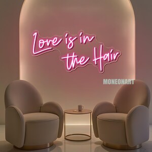 Pu&ograve; includere: Un'insegna al neon rosa con la scritta "Love is in the Hair" &egrave; montata su una parete rosa. Due poltrone beige si fronteggiano, con un tavolino rotondo e una tazza in mezzo. L'insegna &egrave; sopra le sedie.
