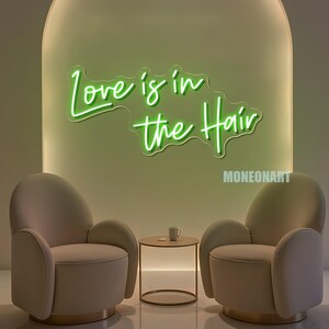 Pu&ograve; includere: Un'insegna al neon verde con la scritta "Love is in the Hair" &egrave; montata su una parete verde chiaro. Due poltrone beige si fronteggiano, con un tavolino rotondo e una tazza tra loro. La parola "MONEONART" &egrave; nell'angolo in basso a destra.