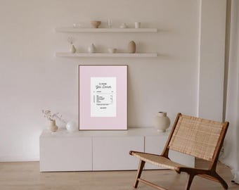 Könnte beinhalten: Ein gerahmter Druck mit rosa Rand, der ein schwarz-weißes Quittungsdesign zeigt. Der Druck befindet sich auf einem weißen Schrank, mit einem Holzstuhl und dekorativen Gegenständen im Hintergrund. Der Text auf der Quittung ist lesbar.
