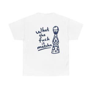 May include: A white short-sleeve t-shirt featuring a dark blue graphic on the back. The design includes a stylized illustration of a tequila bottle next to the text "What the fuck is matcha" written in a casual, hand-lettered dark blue font.