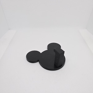 May include: A black, 3D-printed wall hook shaped like Mickey Mouse's head. The hook is on the right side. The hook is designed for hanging items on a wall. The dimensions are in centimetres.