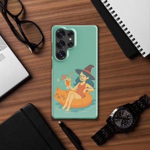 Può includere: Custodia per telefono turchese con una strega dei cartoni animati che si rilassa su un galleggiante a forma di gatto, con in mano un cocktail. La strega indossa un costume da bagno rosso e un cappello a punta. Il galleggiante è arancione.