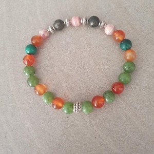 Peut inclure: Un bracelet de perles multicolores avec des perles rondes vertes, oranges, roses et grises. Le bracelet est monté sur un élastique et comprend des perles d'espacement argentées.