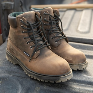 May include: A pair of brown leather work boots with black laces and a black sole. The boots are labeled "Golden Retriever" and "Waterproof". The boots are designed for rugged outdoor use and are likely made for construction or similar work.