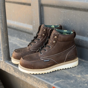 Könnte beinhalten: Ein Paar braune Leder-Arbeitsstiefel mit weißen Nähten und Sohlen. Die Stiefel haben schwarze Schnürsenkel, Metallösen und das Wort "WATERPROOF" ist sichtbar. Die Stiefel sind mit "Golden Retriever" beschriftet.