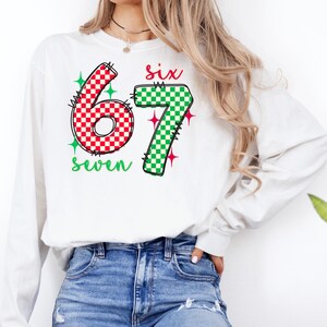 A woman wearing a white long-sleeved shirt with a graphic design featuring the number 67 and the text "Six seven" printed on it.